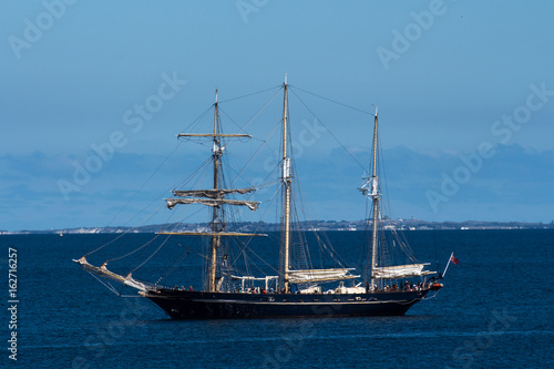 Schooner sailing ship boat moored in ocean bay against blue sky