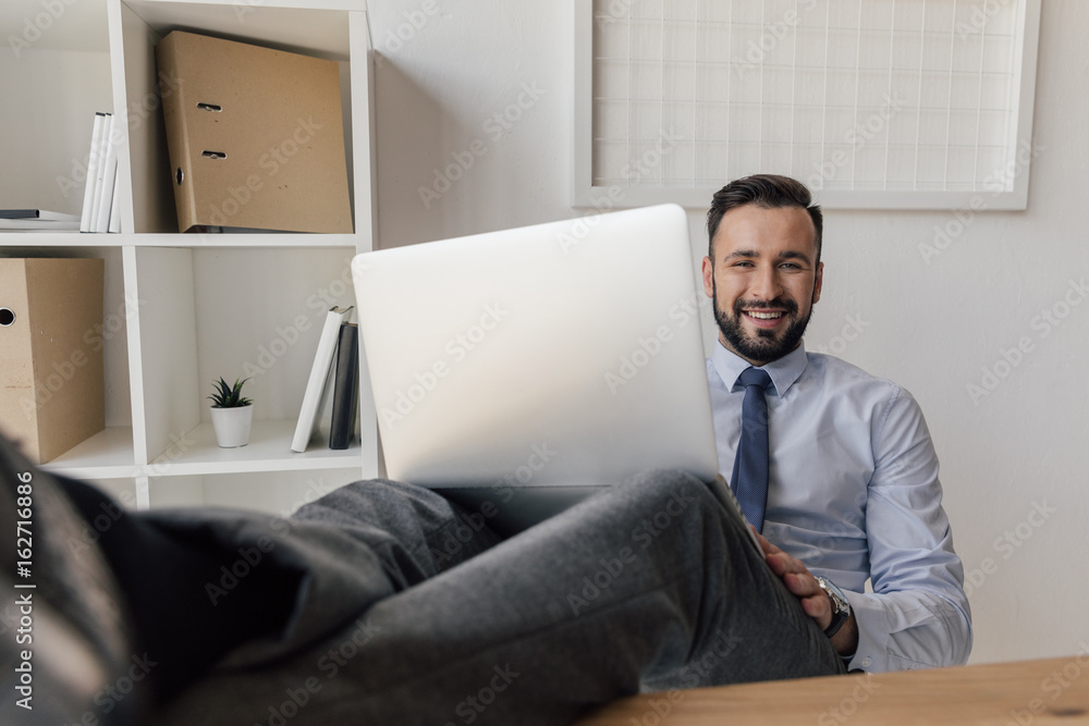 portrait of smiling businessman sitting with laptop on legs and looking at camera portrait of smiling businessman sitting with laptop on legs and looking at camera