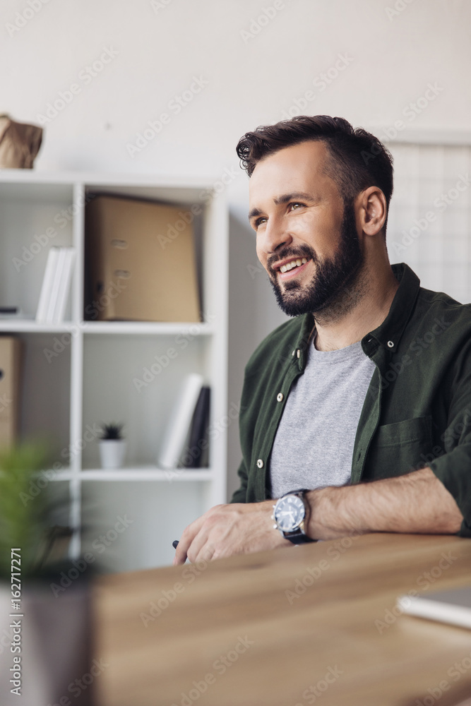 Handsome bearded man smiling and looking away in office Handsome bearded man smiling and looking away in office