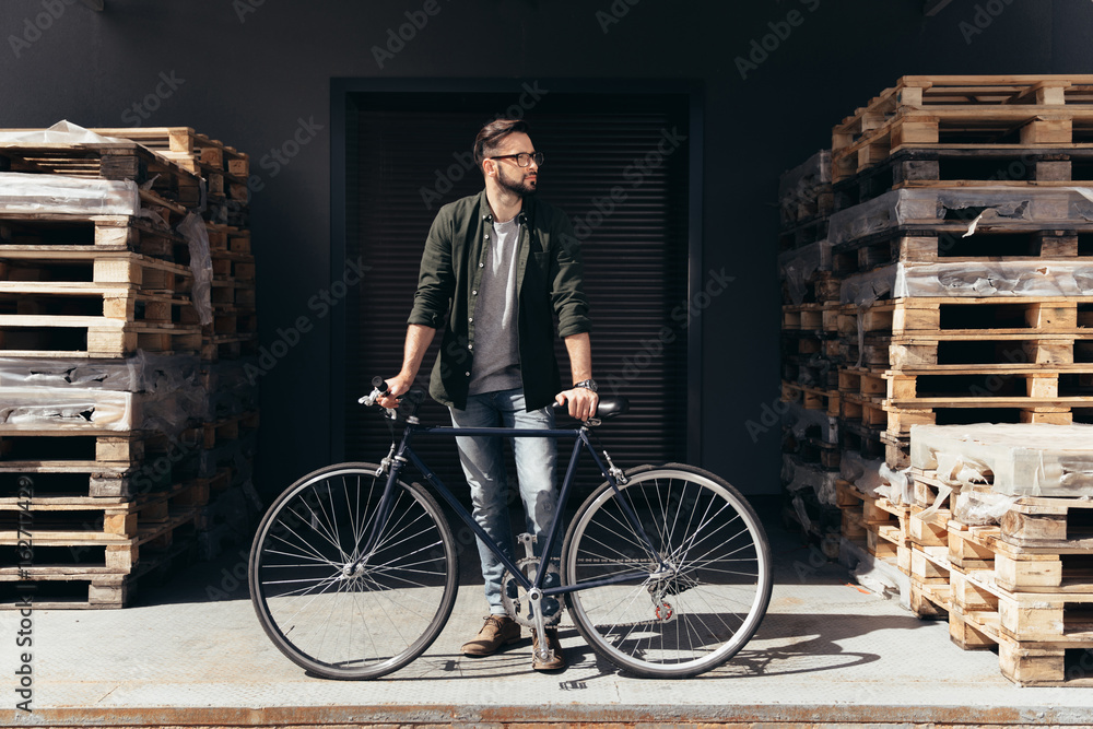 Stylish young man standing with bicycle and looking away Stylish young man standing with bicycle and looking away