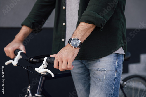 cropped view of young man with watch standing with bicycle