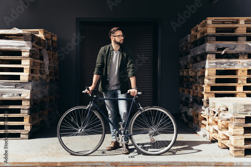 Stylish young man standing with bicycle and looking away
