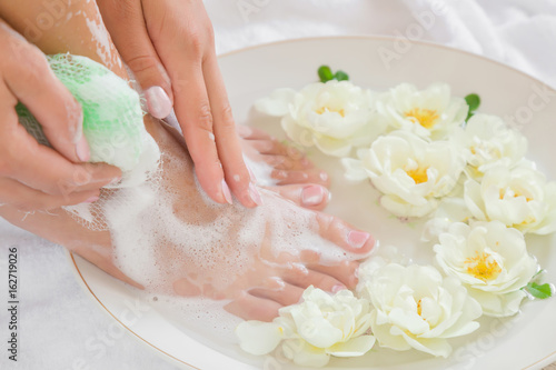 Woman washing her legs in the bow in the bathroom. Cares about a clean and soft skin with body creams  lotions or oils after shower and shaving. Fresh and fragrant white roses in the water.