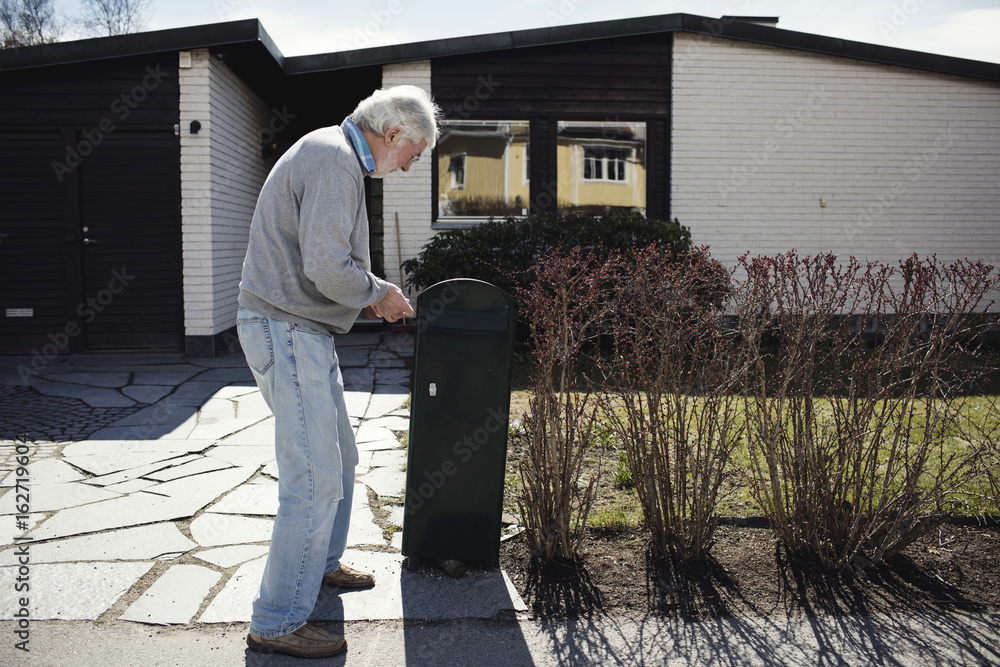 Full length of senior man standing by mailbox outside house during sunny day Full length of senior man standing by mailbox outside house during sunny day