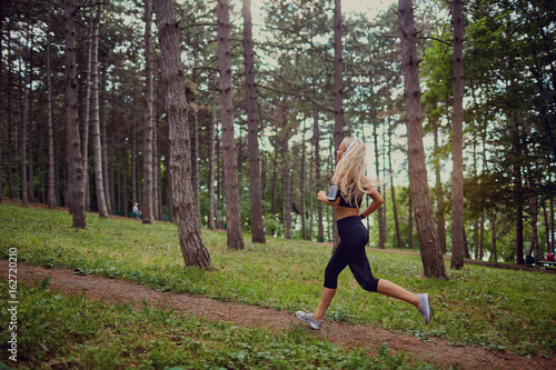 A sporty blonde woman runs through the forest.