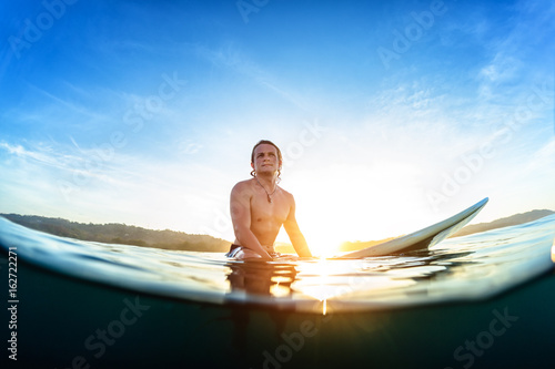 Photography Young man sits on the surfboard in the ocean and waits wave during his sunrise s
