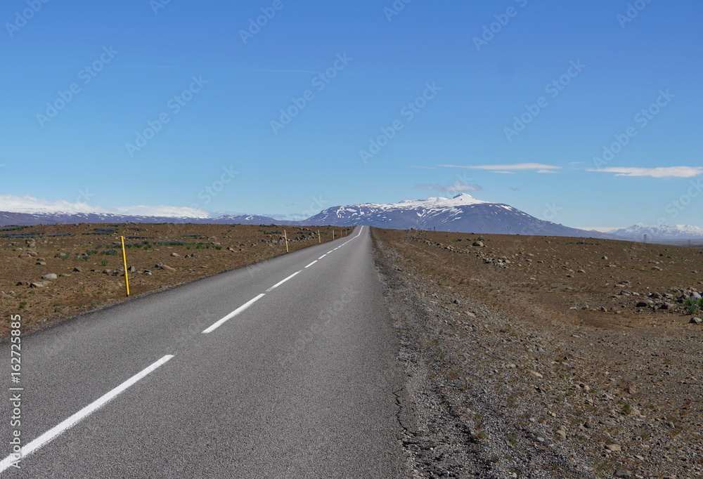 Long asphalt road F35 in the central Iceland between brown fields and in front of high Icelandic mountains