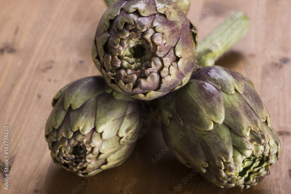 three green and fresh artichokes on the table, ready to be cooked three green and fresh artichokes on the table, ready to be cooked