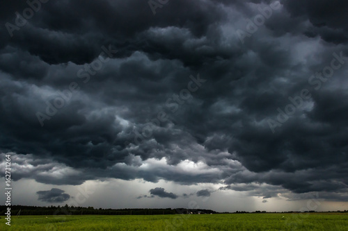 Photography Storm clouds with rain over meadow with yellow grass