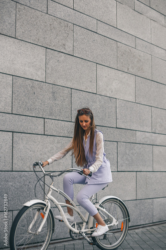 Beautiful young woman getting to work by bike. Beautiful woman in a purple suit on a white bicycle.