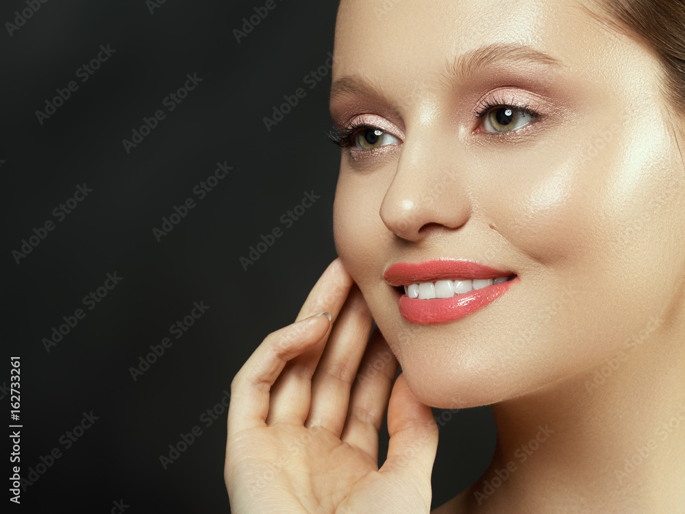 Fototapeta premium Nude makeup. Beauty woman face portrait. Beautiful spa model girl with perfect clean skin. Female looking at camera and smiling. Youth and skin care concept. Isolated on a dark gray background