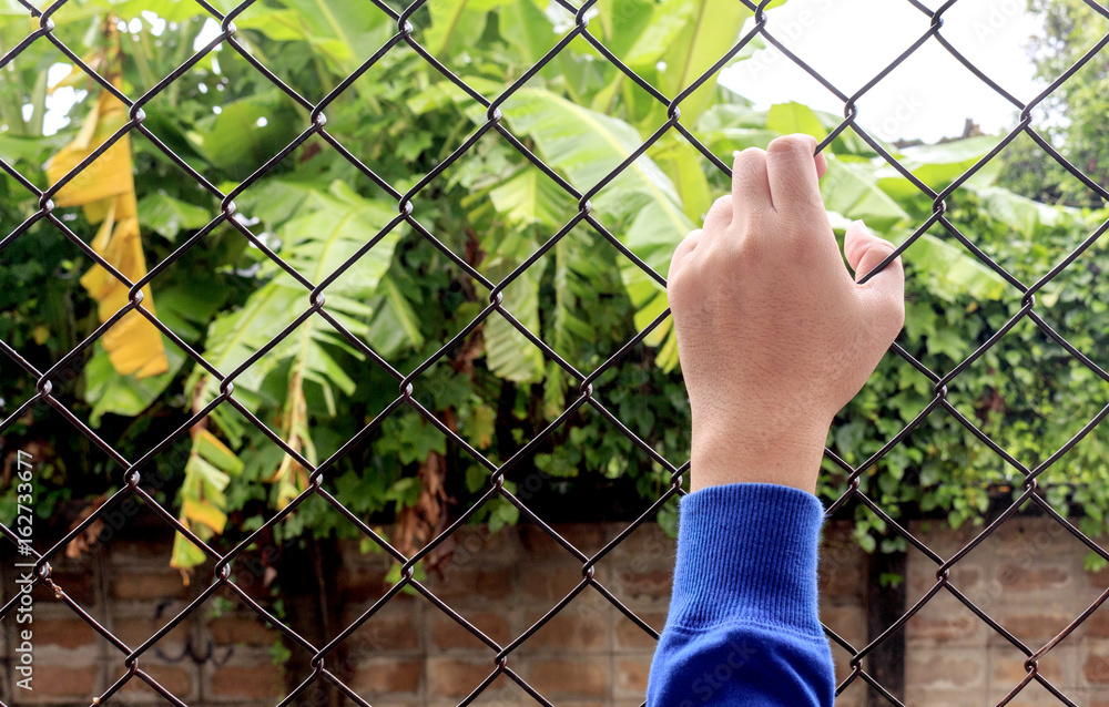 closeup hand grabs the fence with soft-focus and over light in the background closeup hand grabs the fence with soft-focus and over light in the background