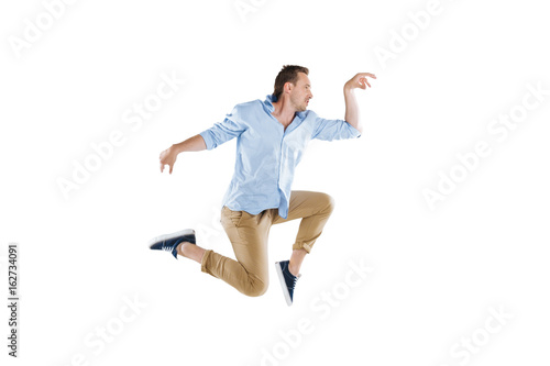 side view of young man jumping and looking away isolated on white