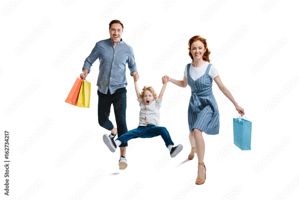 Obraz premium Happy young family with one child holding shopping bags and smiling at camera isolated on white