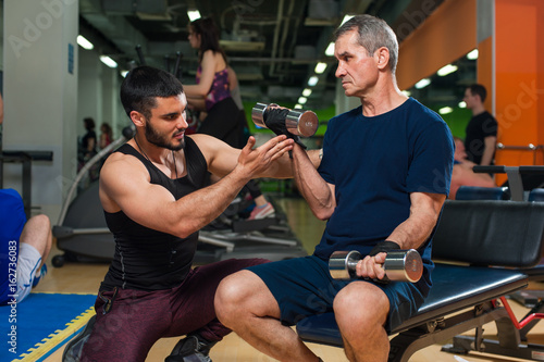 Senior man working in gym with personal trainer