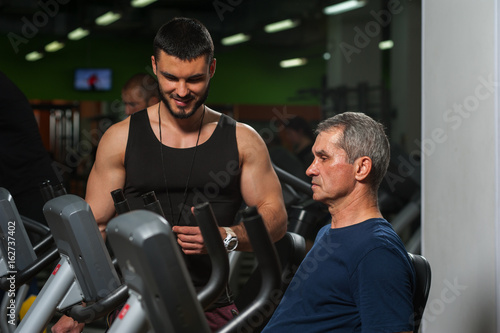 Senior man on machine and his personal trainer