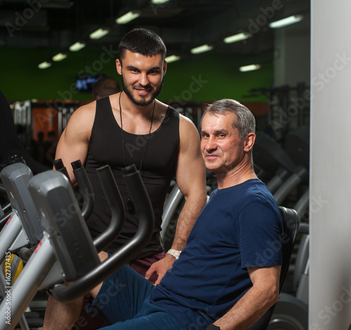 Senior man exercising with trainer in gym