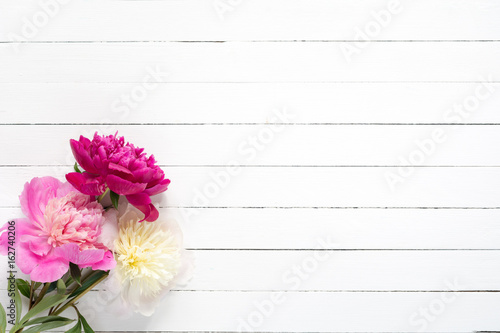 Peonies on white wooden planks background with copy space, top view. Great use as mock up for products, feminine design projects, wedding / invitation / holiday cards and so on