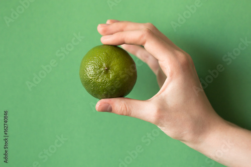 Fresh juicy tasty green lime in a human hand on green background