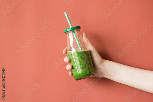 Woman hand holding smoothie shake against colored wall. Drinking green healthy smoothie concept.