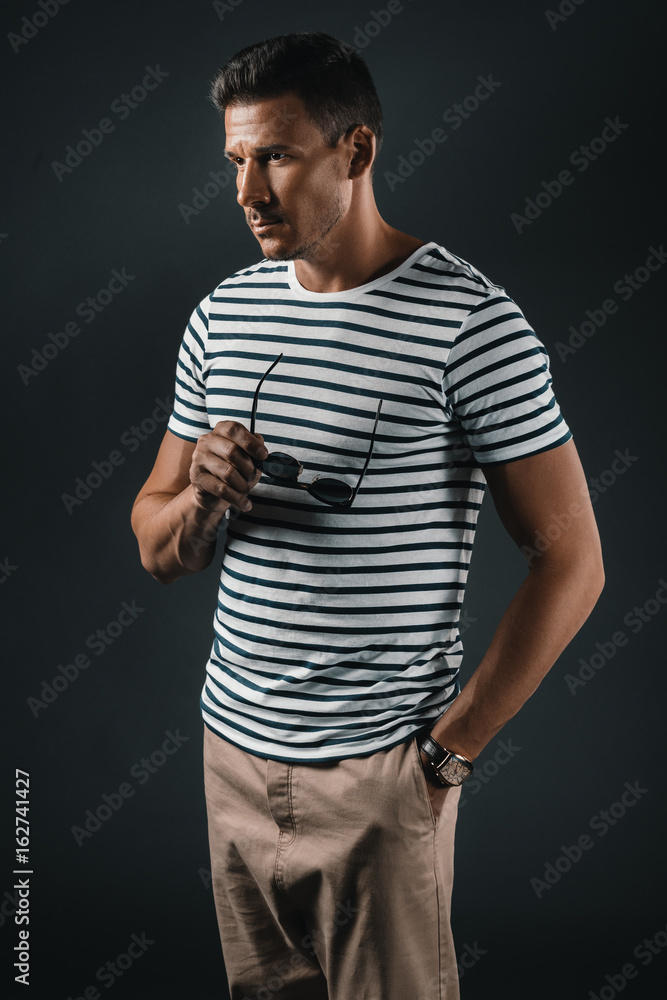 Handsome stylish man holding sunglasses while standing with hand in pocket and looking away Handsome stylish man holding sunglasses while standing with hand in pocket and looking away