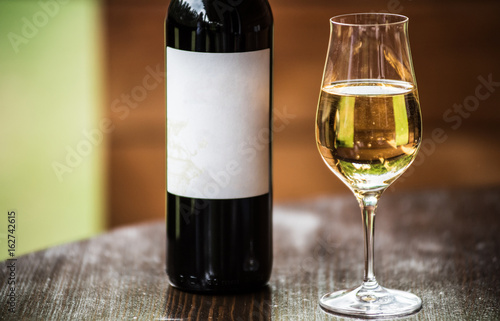 A glass with a white wine and the black wine bottle with label. Selective focus.