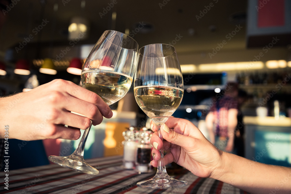 Young couple with glasses of white wine on a date in a cozy Italian restaurant. Leisure, drinks, people and holidays concept - happy man and woman clinking glasses.