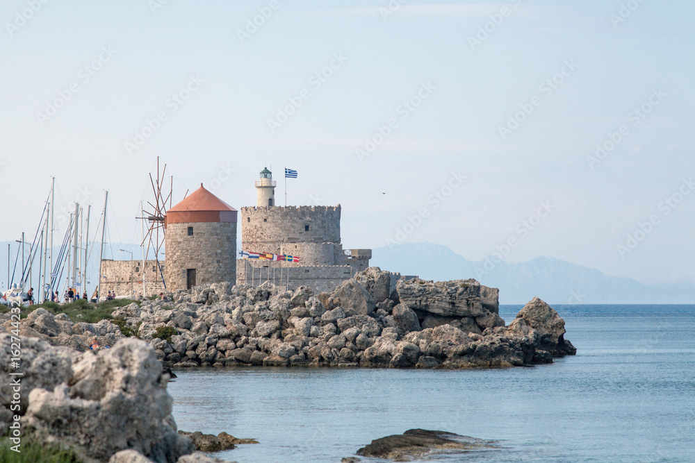 Santa Claus Fortress on the pier in Mandraki Harbor. Bastion of defense on the quay of Rhodes. Harbor and monuments in Rhodes. Old defensive walls and windmills.