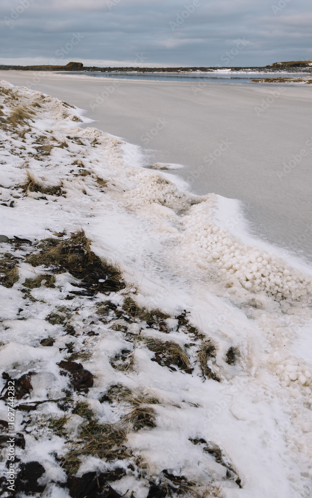 Winter Icelandic road by the lake covered in ice and frozen grass, sunset view, kalfshamarsvik Winter Icelandic road by the lake covered in ice and frozen grass, sunset view, kalfshamarsvik