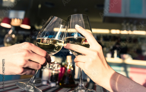 Young romantic couple with glasses of white wine on a date in a cozy Italian restaurant. Leisure, drinks, people and holidays concept - happy man and woman clinking glasses.