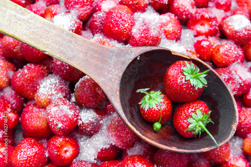 Against a background of strawberries with sugar a wooden spoon for jam. photo