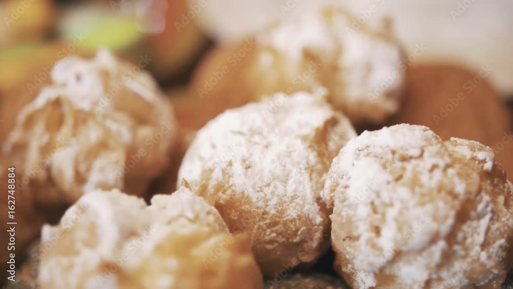 Hand manages profiteroles covered in sugar powder in pile on plate in confectionery, close up dolly shot Hand manages profiteroles covered in sugar powder in pile on plate in confectionery, close up dolly shot