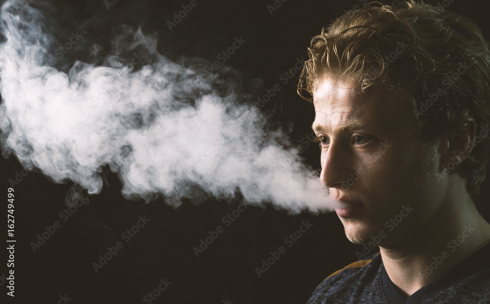 Isolated young man holding and vaping an electronic cigarette or e cig.