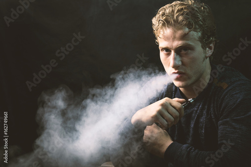 Isolated young man holding and vaping an electronic cigarette or e cig.