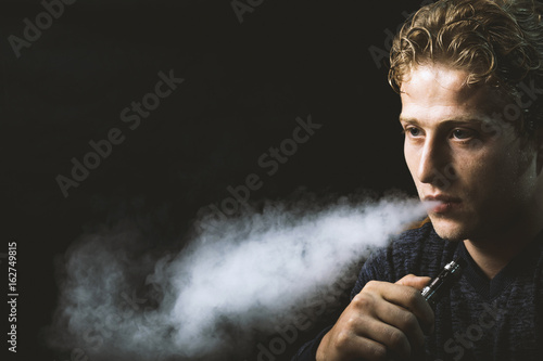 Isolated young man holding and vaping an electronic cigarette or e cig.
