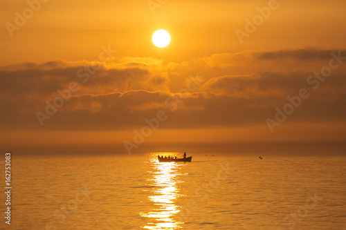 Fishermen on a boat fishing on a sea with beautiful sunrise in background