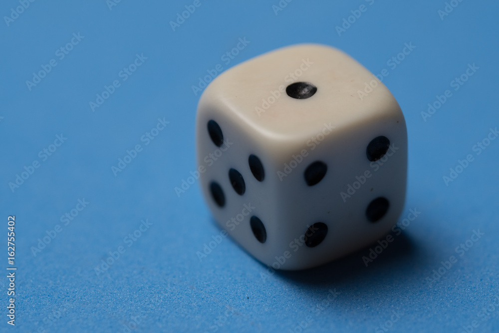 Closeup of single white cubic dice isolated over blue background Closeup of single white cubic dice isolated over blue background