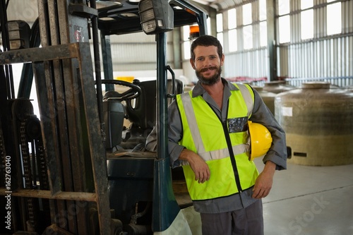 Smiling worker leaning on forklift in factory