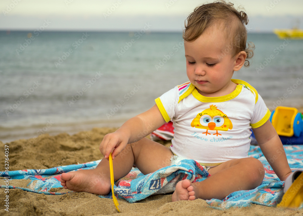 Little cute baby playing with sand near the sea at sunset Little cute baby playing with sand near the sea at sunset