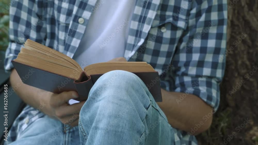 Close up of a young man with book sitting in the park. People stock footage shot at summer season time. Close up of a young man with book sitting in the park. People stock footage shot at summer season time.