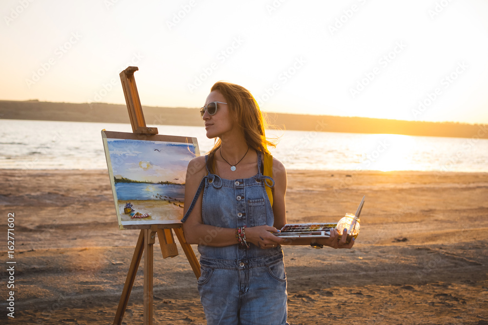 Obraz premium Young woman artist painting landscape in the open air on the beach
