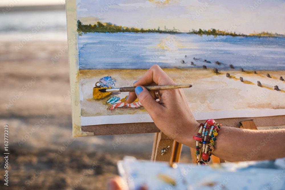 Obraz premium Young woman artist painting landscape in the open air on the beach, close up
