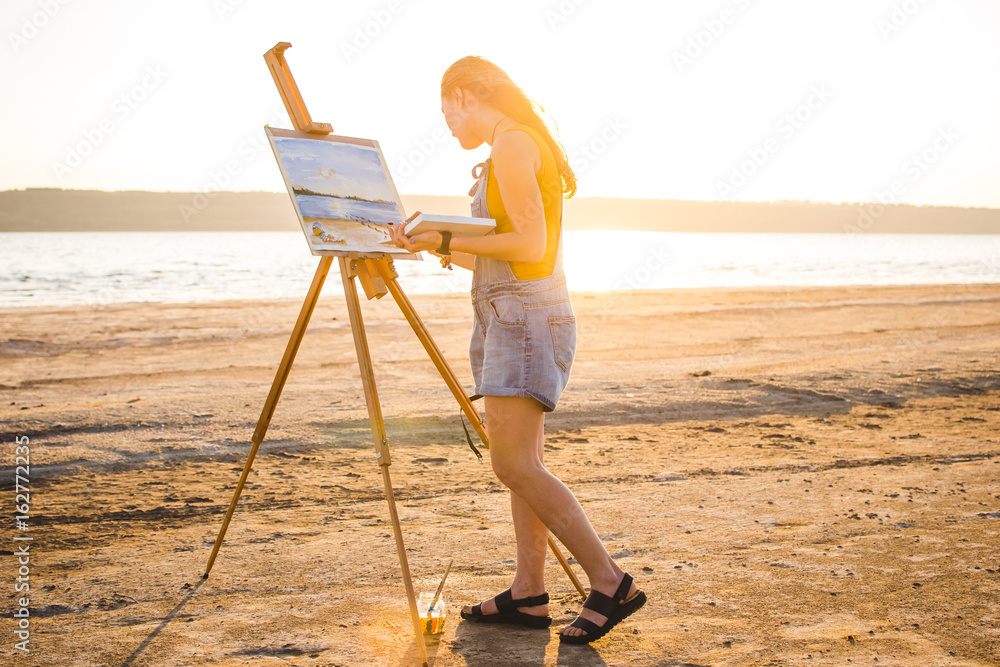Naklejka premium Young woman artist painting landscape in the open air on the beach