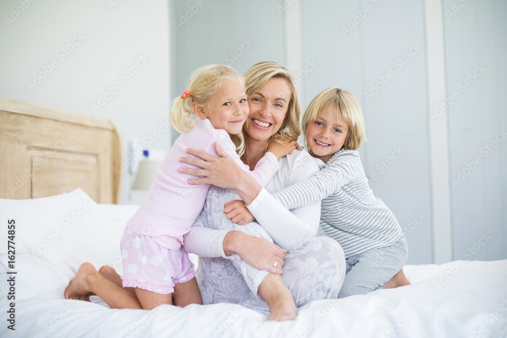 Portrait of smiling kids embracing her mother in bedroom Portrait of smiling kids embracing her mother in bedroom