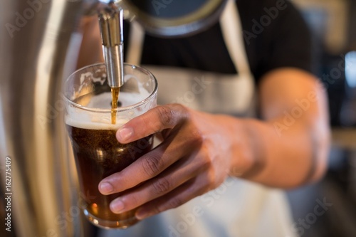 Midsection bartender pouring beer from tap