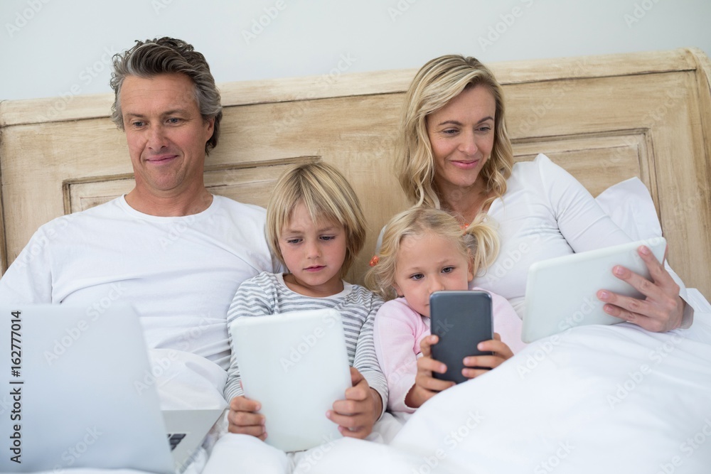 Family using digital tablet, mobile phone and laptop on bed in t Family using digital tablet, mobile phone and laptop on bed in t