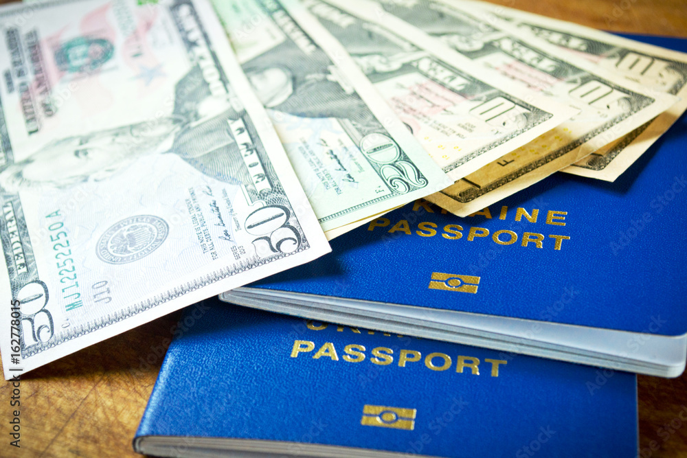 Dollars and two blue passports for travel on wooden table, close-up Dollars and two blue passports for travel on wooden table, close-up