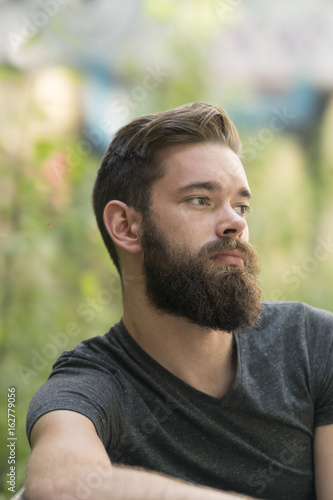 Handsome thoughtful bearded guy sitting on a bench in park