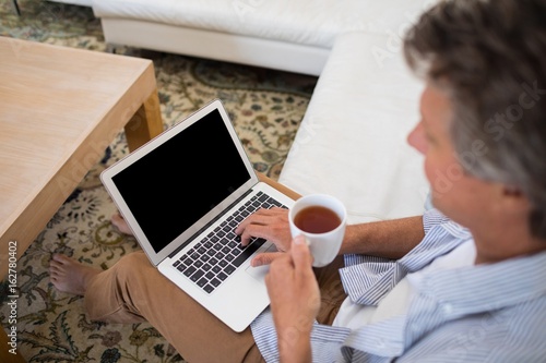 Man using laptop while having coffee in living room