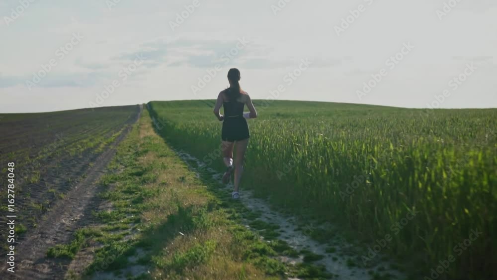 Young woman runner is runing across the field in a sporty uniform. Slow motion Young woman runner is runing across the field in a sporty uniform. Slow motion